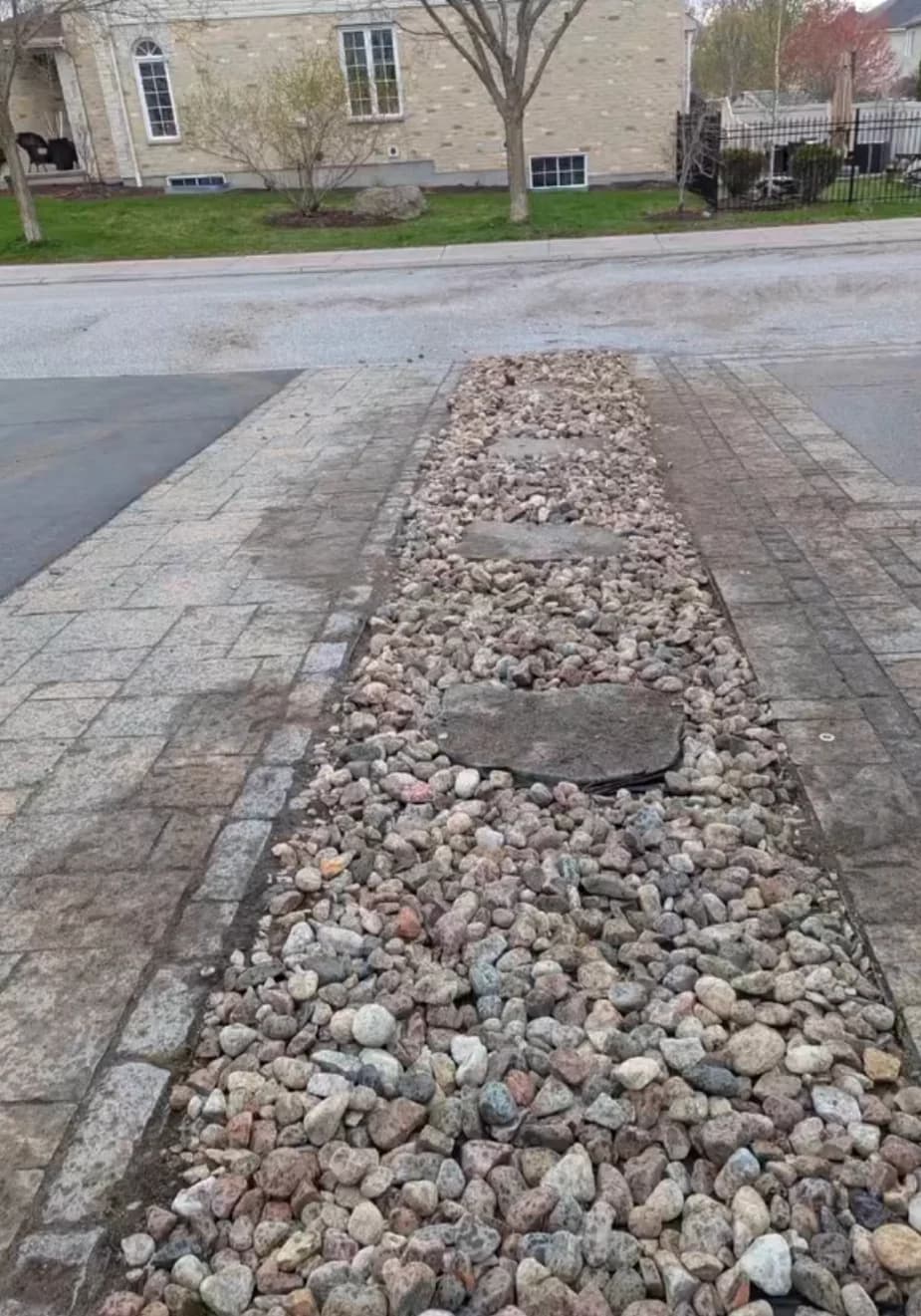 River rock drainage strip with flagstone stepping stones installed between interlock driveway sections