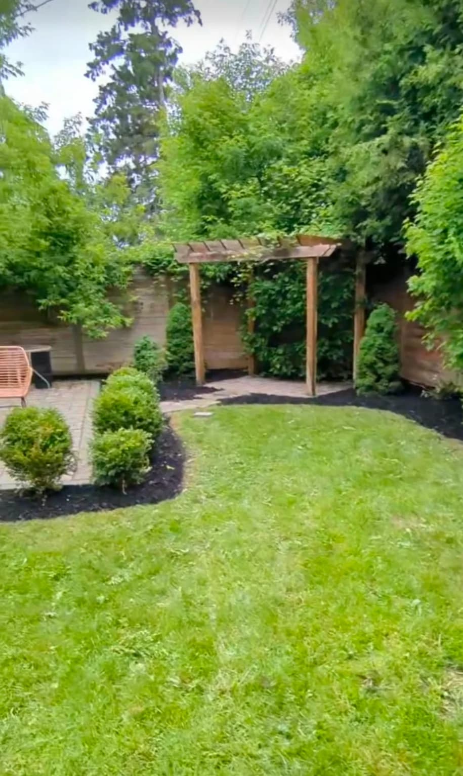 Completed backyard landscaping with wooden garden pergola, patio pavers, manicured turf, and mulch beds