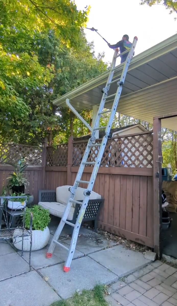 Crew member on a ladder pruning overhanging branches above a backyard patio