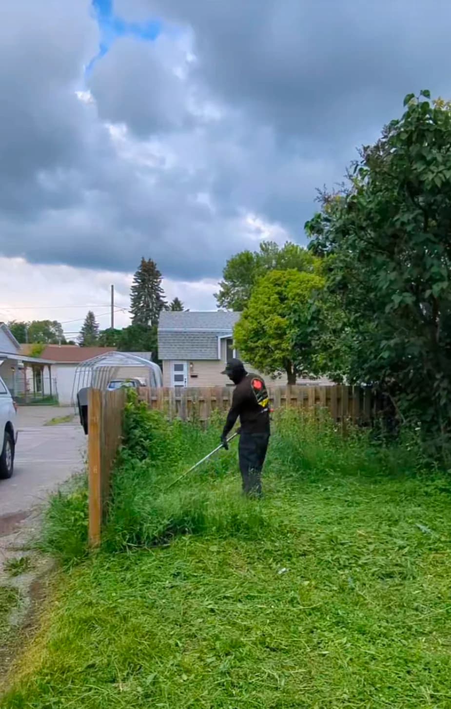 Crew member trimming overgrown grass and weeds tight along a residential backyard fence